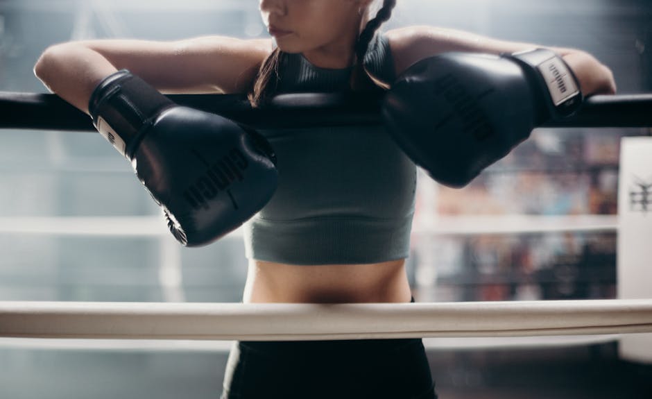Young female boxer resting on the ropes in a boxing gym, emphasizing strength and focus