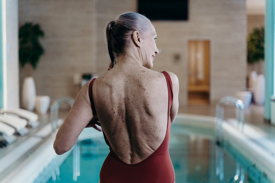 Senior woman in red swimsuit standing at indoor pool side, exuding confidence