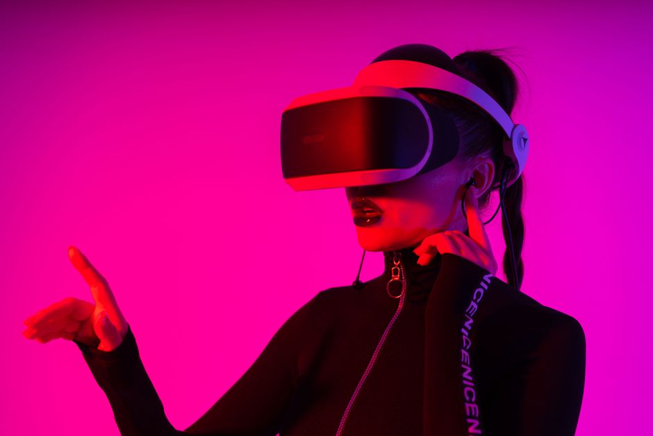 Young female entertaining with virtual reality goggles while playing videogame on pink background in neon light